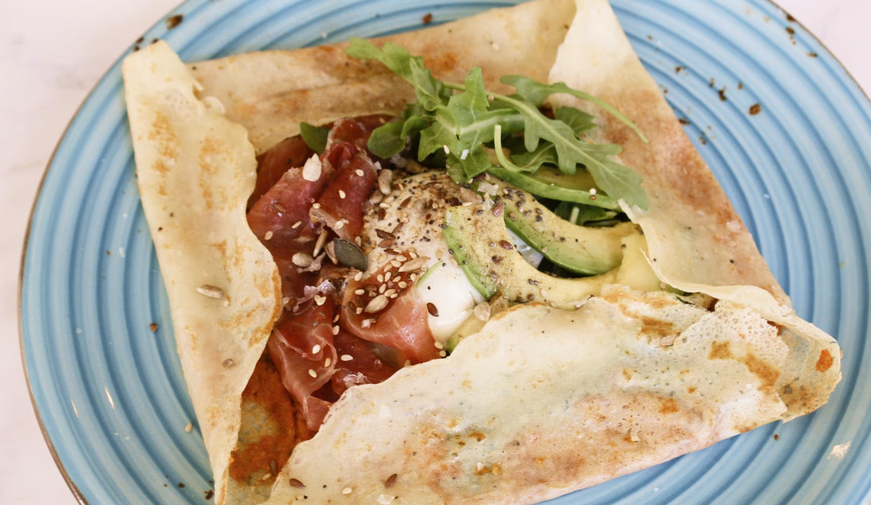 Crepe salada con jamón, aguacate y rúcula en un plato azul
