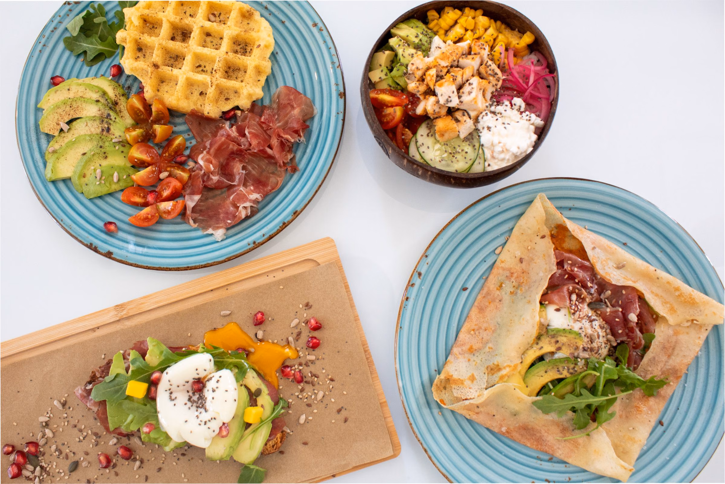 Desayunos de Menta sobre una mesa blanca: gofre salado, poke bowl, tostada con huevo poché y crepe