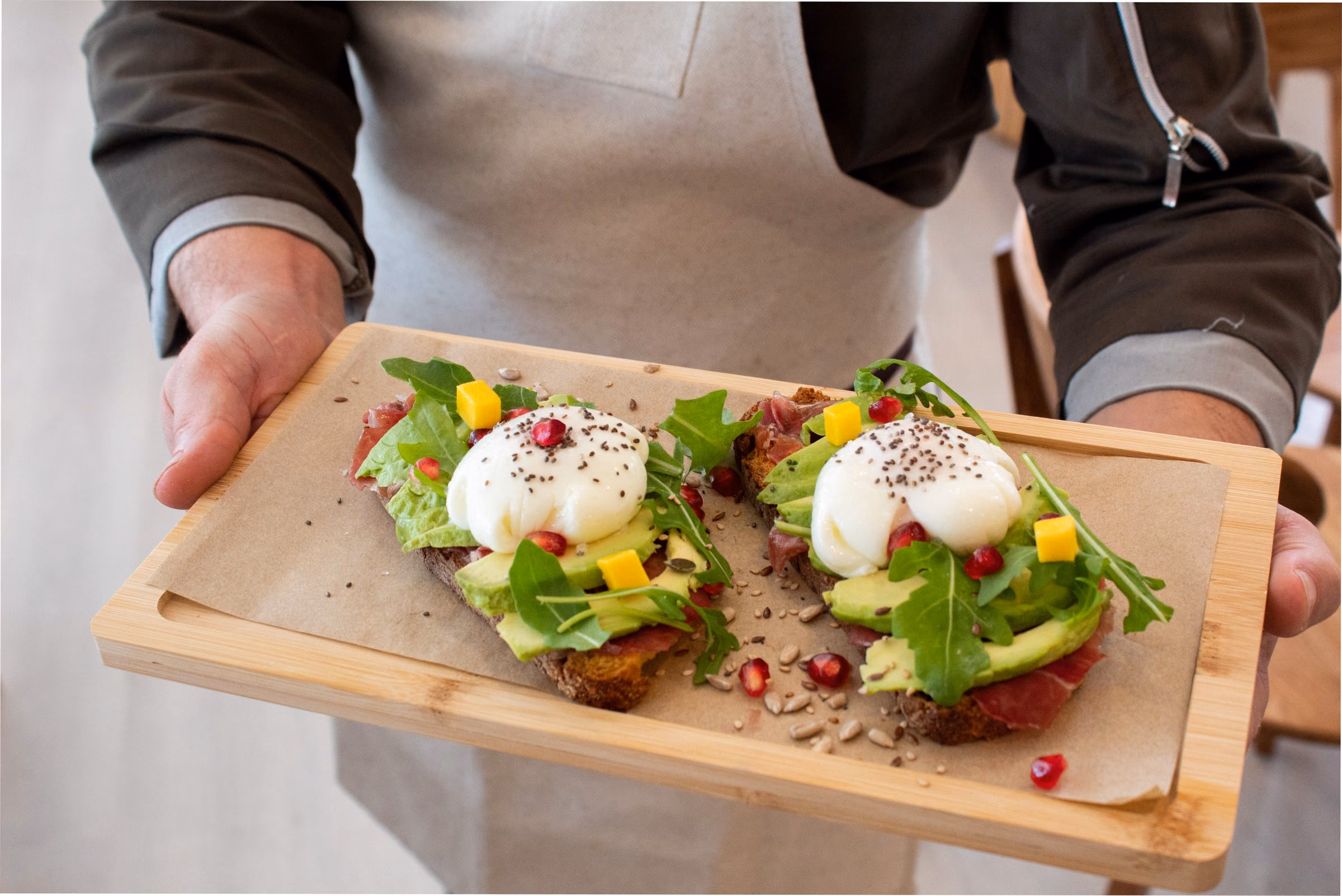 Dos tostadas de aguacate con huevo poché, mango y semillas sobre una tabla de madera